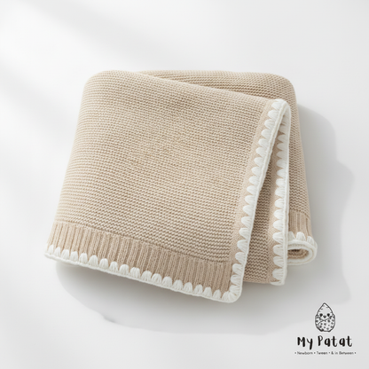 Beige knit baby blanket with white pom-pom trim