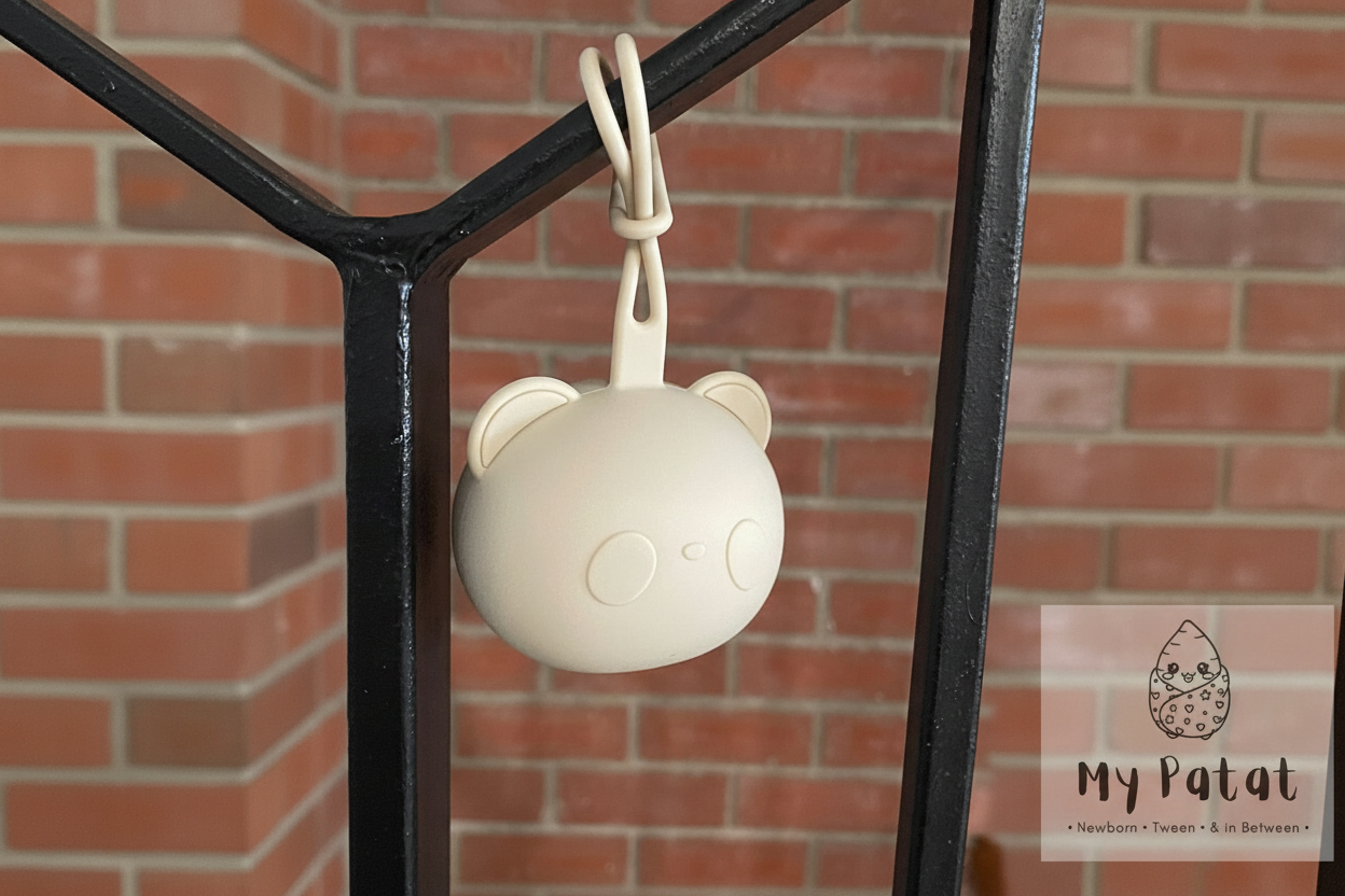 Cream silicone bear soother holder hanging from black iron railing