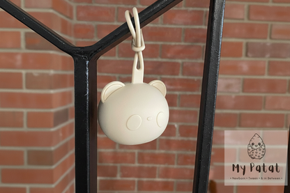 Cream silicone bear soother holder hanging from black iron railing