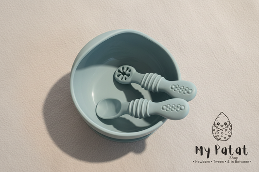 Dusty blue silicone baby spoons resting inside suction bowl top-down view