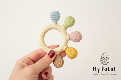 Silicone baby teething ring held in hand on soft white background with My Patat Shop logo