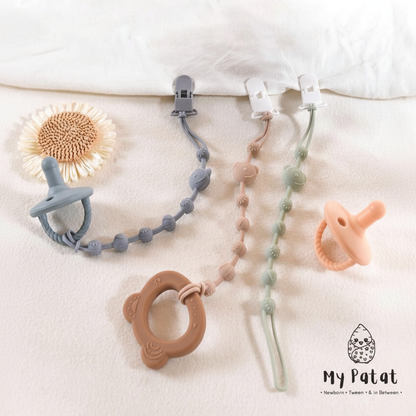 Silicone dummy clip chains on white linen with dried sunflower and teether
