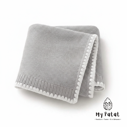 Grey knit baby blanket with white pom-pom trim
