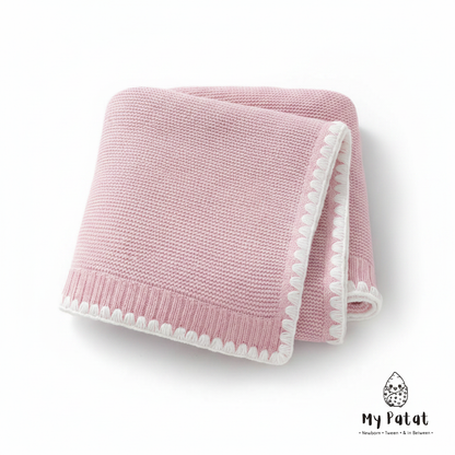 Pink knit baby blanket with white pom-pom trim